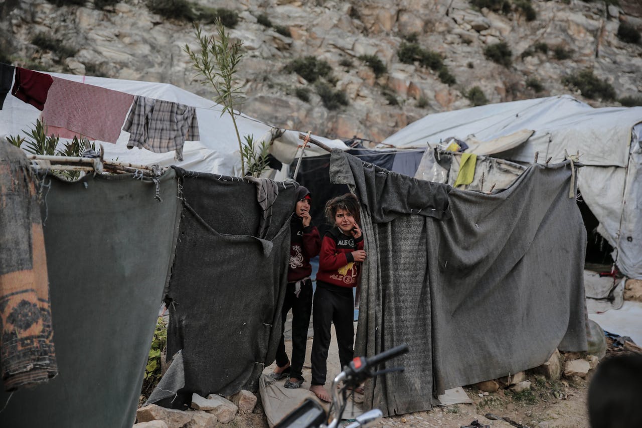 Two children stand outside a makeshift shelter in a Syrian refugee camp, capturing resilience in adversity.